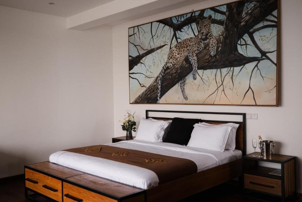 A bedroom with a bed, wooden nightstands, a painting of a leopard on a tree, and a vase with flowers.