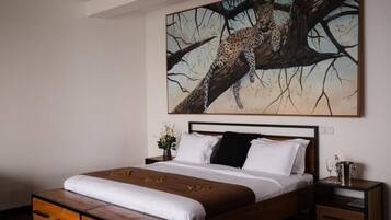 A bedroom with a bed, wooden nightstands, a painting of a leopard on a tree, and a vase with flowers.