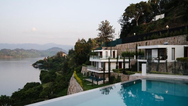 Una villa moderna con piscina con vista a un lago, rodeada de exuberante vegetación y colinas.