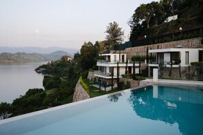 A modern villa with a pool overlooking a lake, surrounded by lush greenery and hills. - Umurobyi Lodge (Bwishyura)