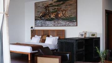 Une chambre d’hôtel avec un lit, un tableau représentant des lions, un meuble noir pour la télévision et d’autres appareils, et une table basse en bois.