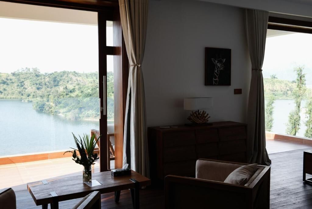 A room with a view of a lake, a wooden table with a plant, a sofa, and a cabinet.