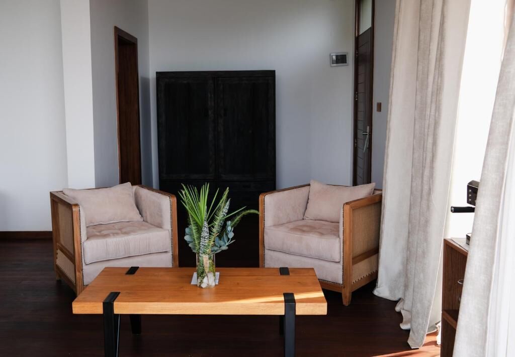 Una habitación con dos sillones color beige, una mesa de madera con una planta y una puerta de madera oscura.