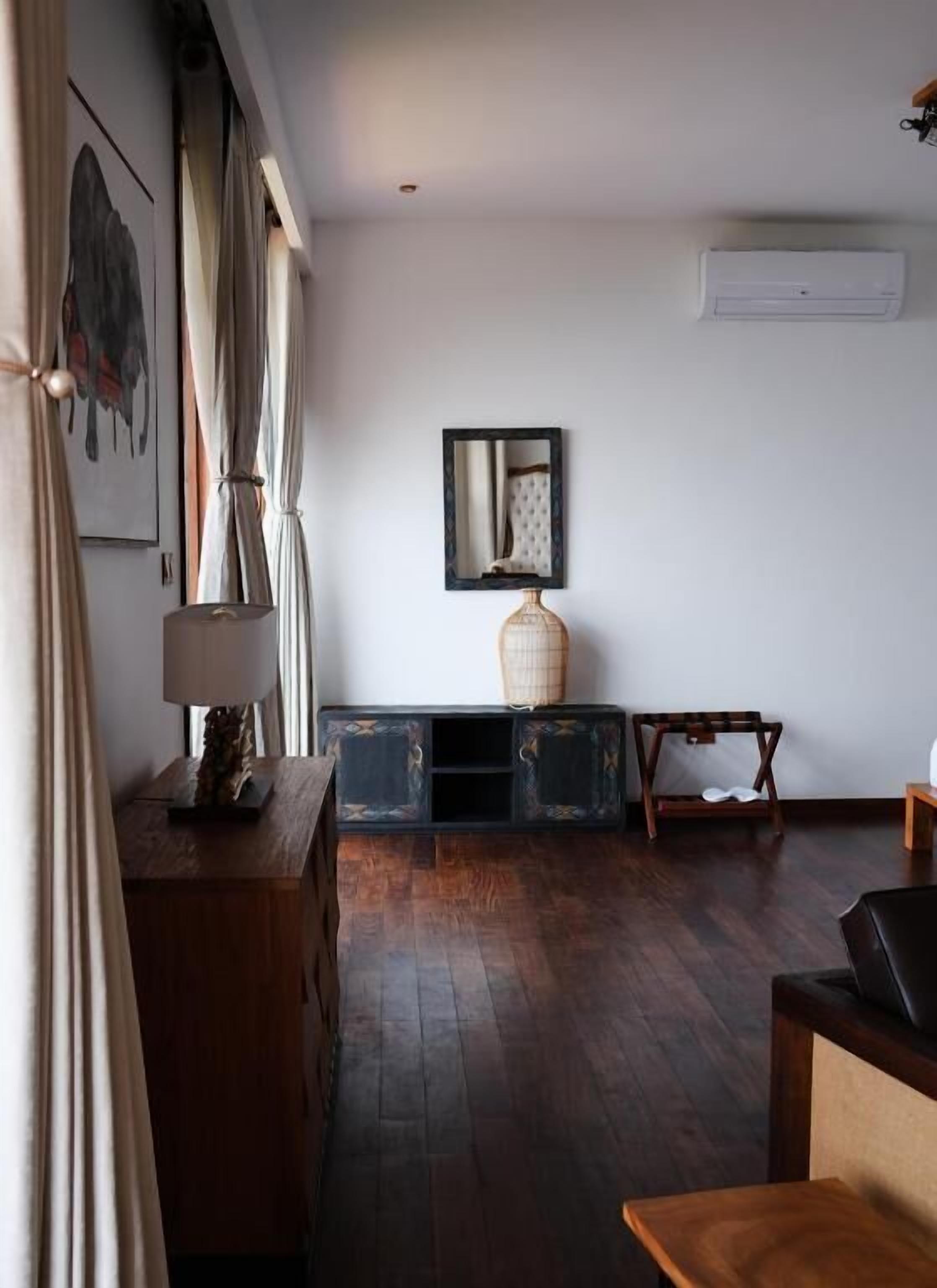 A room with a wooden cabinet, a lamp, a vase, and a mirror on the wall.