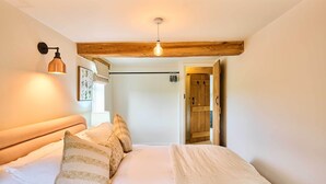 A bedroom with a wooden ceiling, a bed with white bedding, a wall-mounted light, and a door leading to another room. - Host & Stay | The Coral Cottage (Morley Saint Botolph)