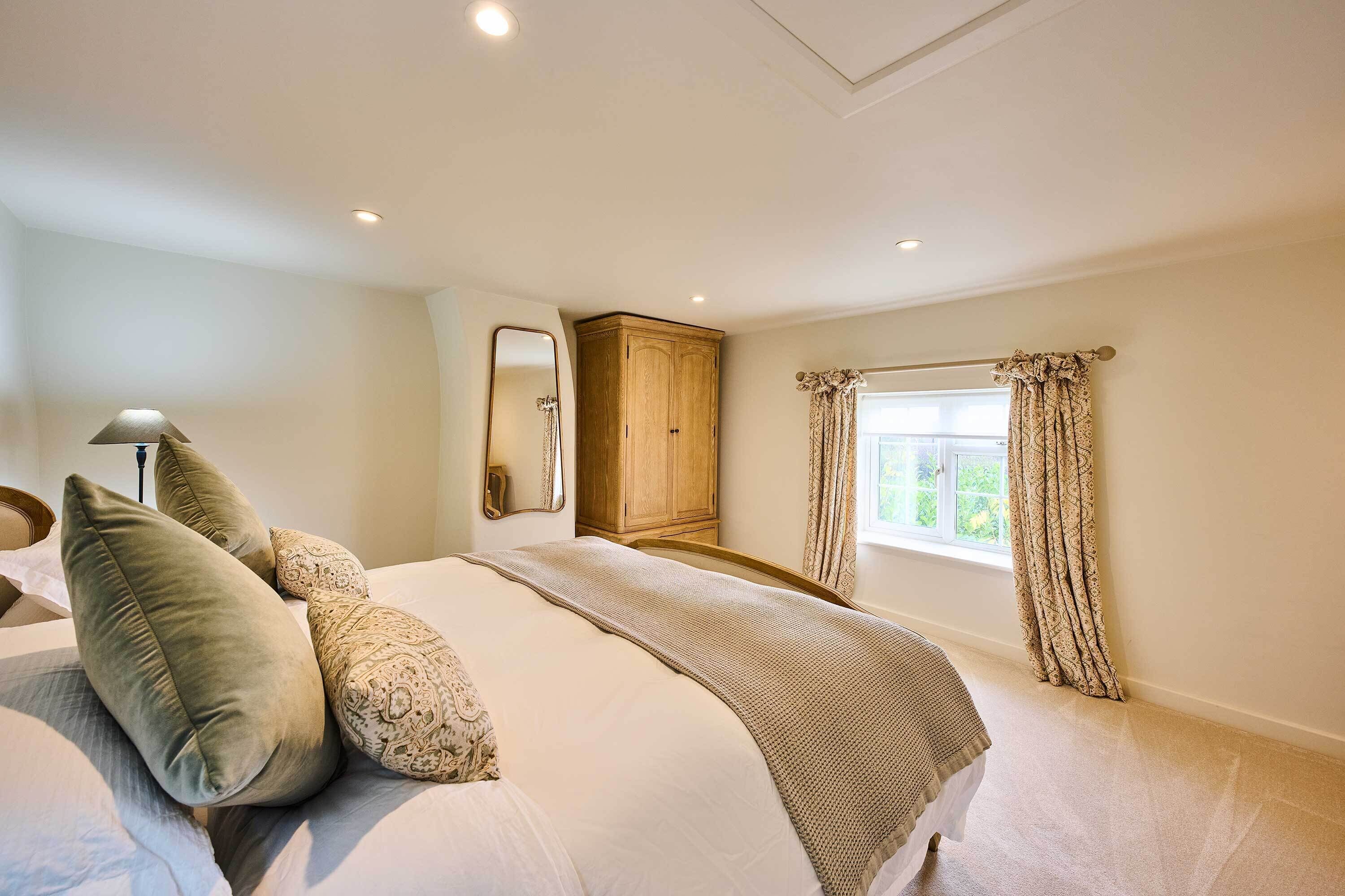 A bedroom with a bed, a wooden wardrobe, a mirror, and a window with curtains.