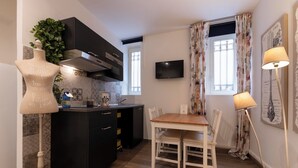 A compact kitchen with dark cabinets, a wooden dining table, and a white chair. - Popolo Rooms&Suites (Rome)