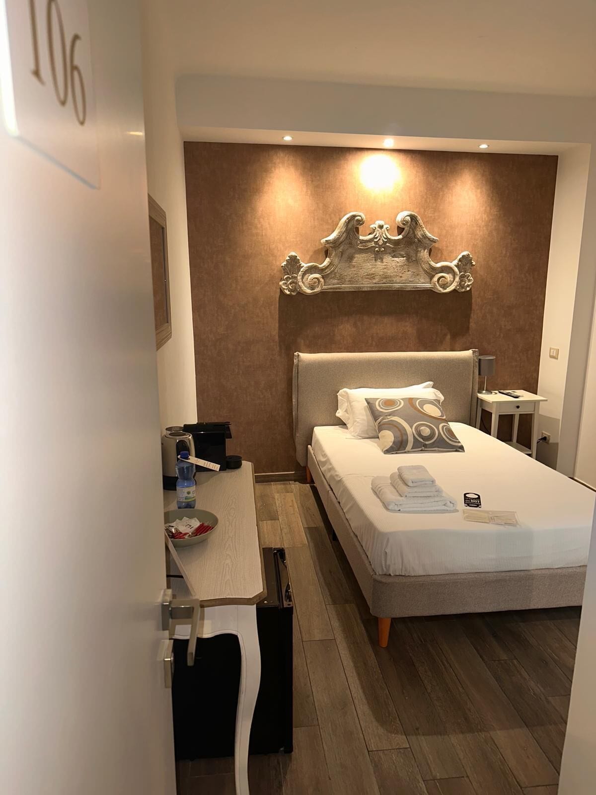 A hotel room with a bed, bedside table, lamp, and a wall-mounted decorative piece.