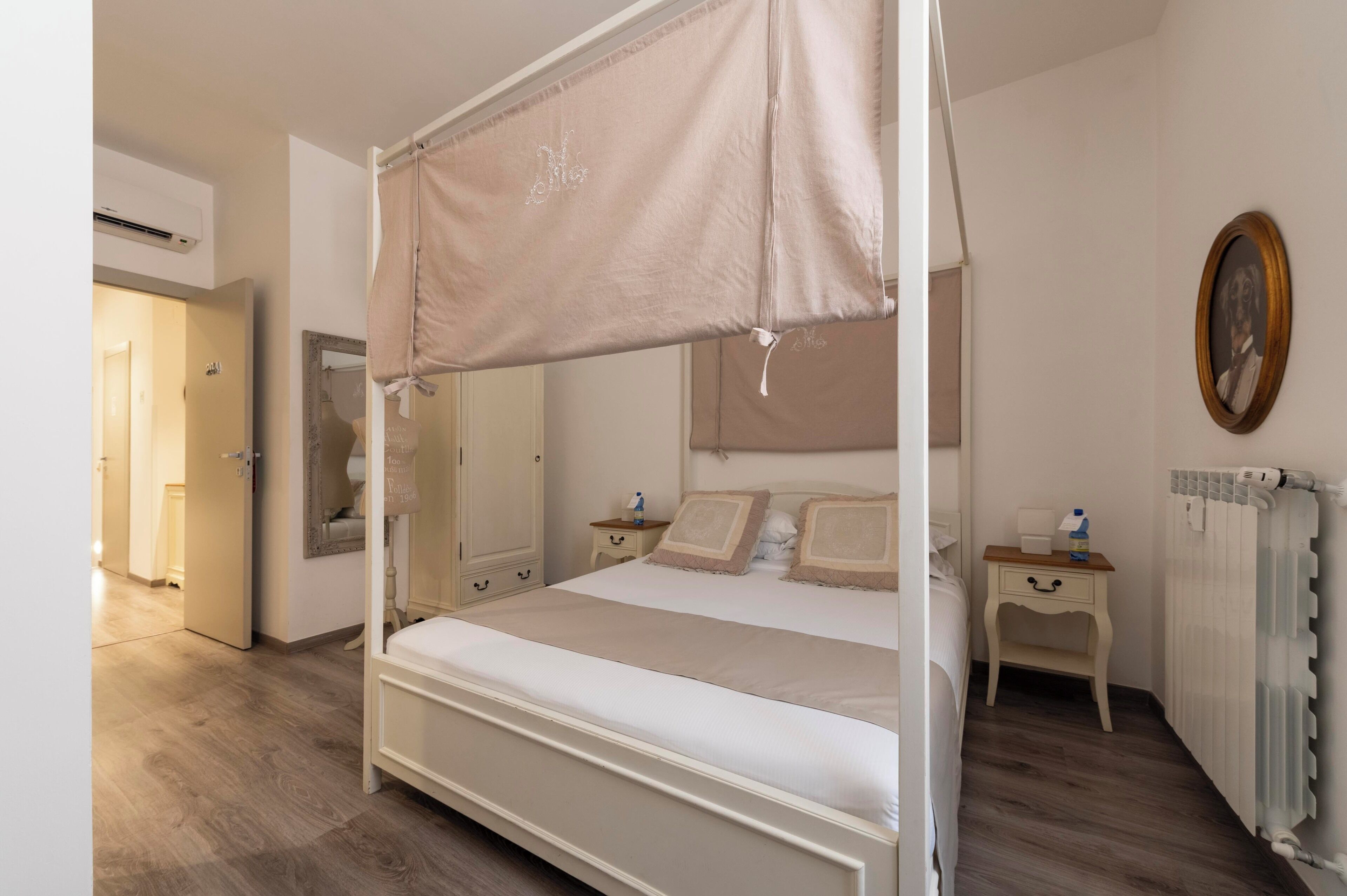A four-poster bed with a canopy, a bedside table with a lamp, a framed picture on the wall, and a radiator.