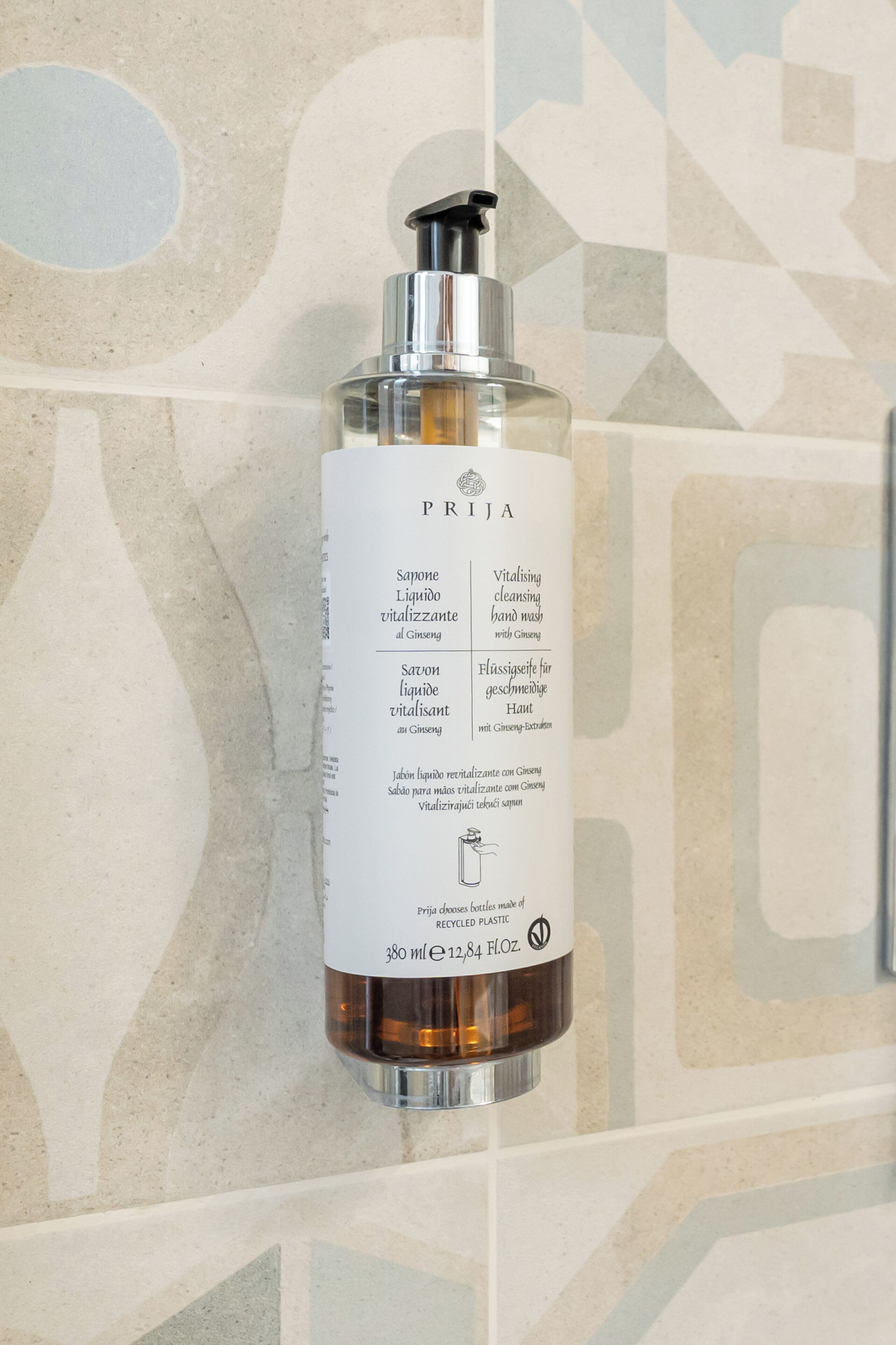 A bottle of PRIJA Vitalizing hand wash with Ginseng on a tiled wall.