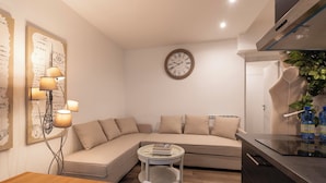 A modern living room with a beige sectional sofa, a round coffee table, and a wall clock. - Popolo Rooms&Suites (Rome)