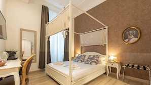 A four-poster bed with a canopy, a bedside table with a lamp, a chair, a desk with a kettle, and a framed picture on the wall. - Popolo Rooms&Suites (Rome)