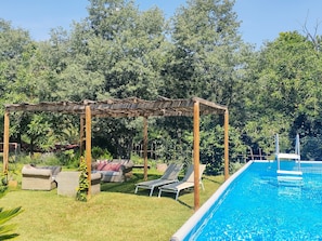 Un área de piscina con pérgola, sillas de descanso y un espacio cubierto para sentarse.