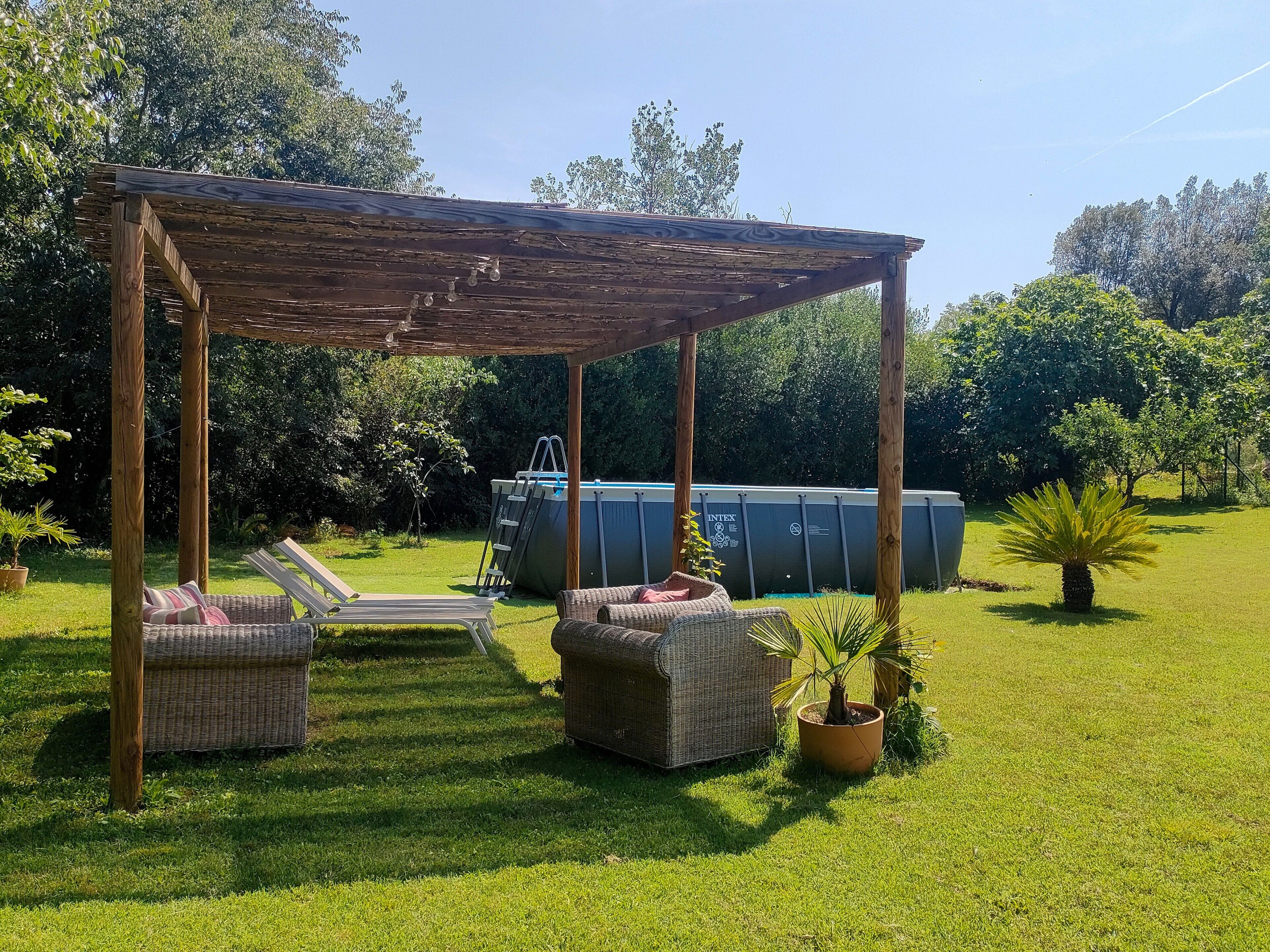 Ein überdachter Außenbereich mit Korbmöbeln, einem Pool und einem Garten.