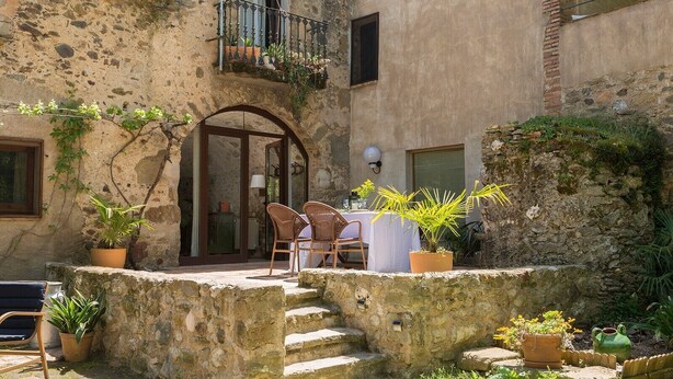 Un bâtiment en pierre doté d’un balcon, d’une table avec des chaises et de plantes en pot.