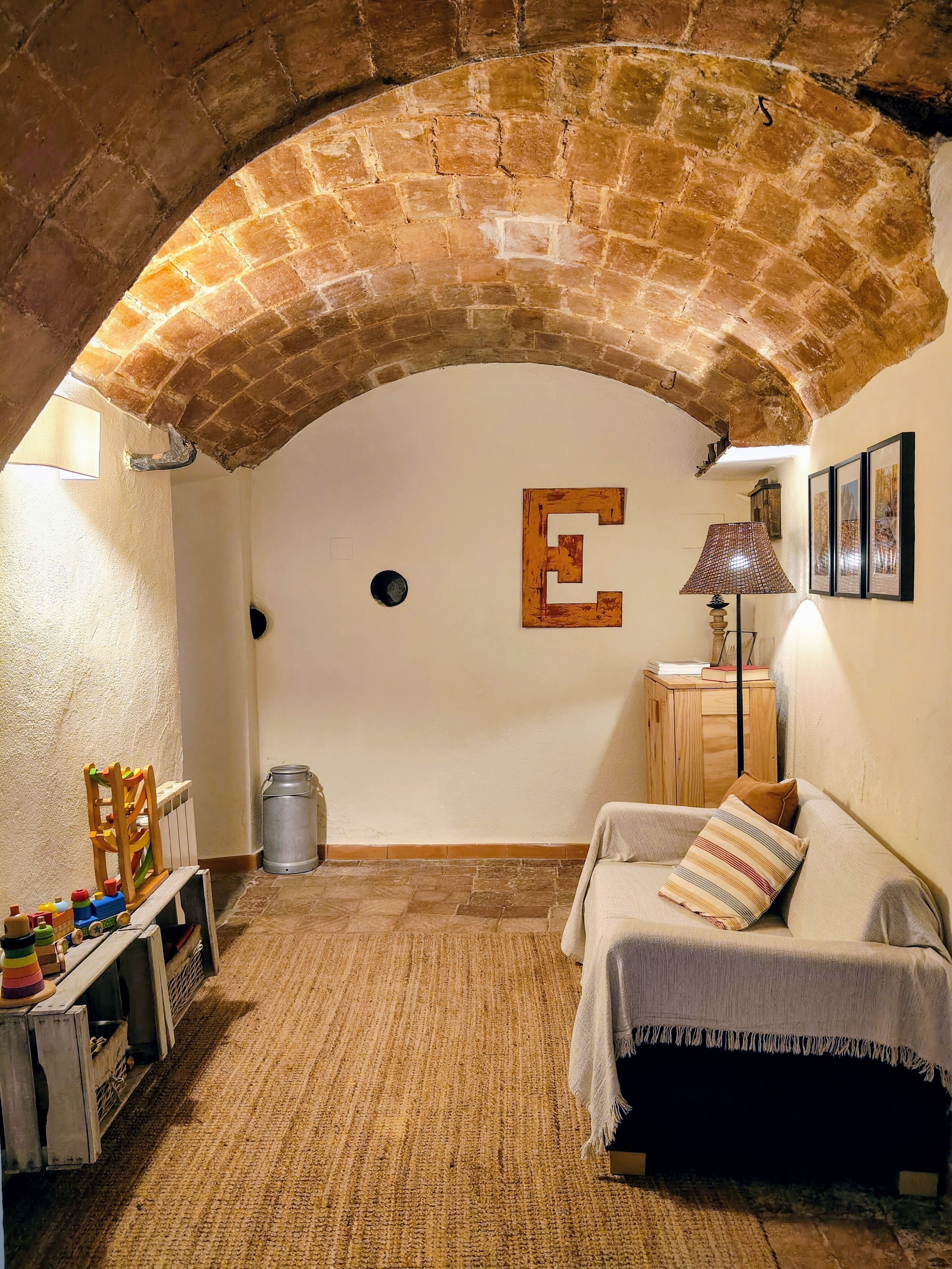 Een kamer met een plafond van natuursteen, een bed met een gestreept kussen, een klein tafeltje met een lamp, een radiator en een houten stoel met speelgoed.
