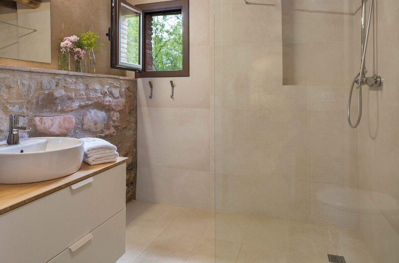 A bathroom with a stone wall, a white sink, a window, and a shower.