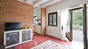 Een kamer met een bakstenen muur, een televisie op een kast, een keukenhoek en een schuifdeur naar buiten.