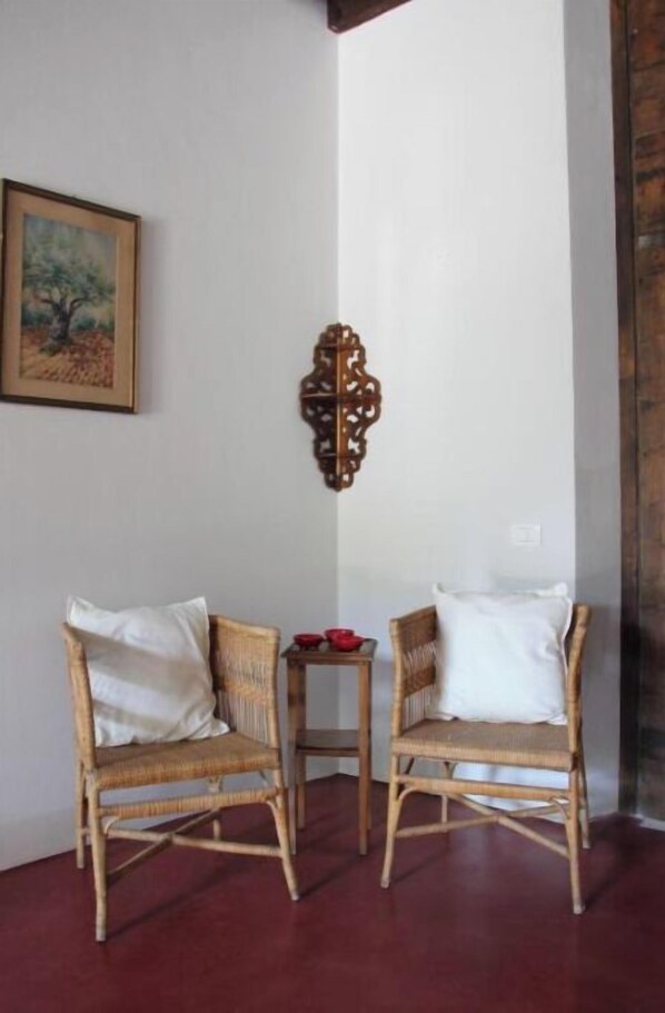 A corner room with two wicker chairs, a small table with red bowls, and a framed painting on the wall. - Relais Villa Ambrosetti - Elegant Suite with a View of the Garden in Verona (Avesa)