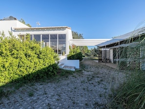 Ein modernes Haus mit großem Panoramafenster, einer überdachten Terrasse und einem Schotterweg.