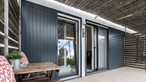 Eine moderne Außenpatio mit Holztisch und -stühlen, einem Topfpflanzen und einer Glastür, die in einen Innenbereich führt.