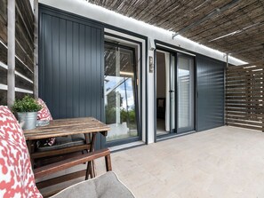 Um pátio moderno ao ar livre com mesa e cadeiras de madeira, um vaso com planta e uma porta de correr de vidro que dá para o interior.