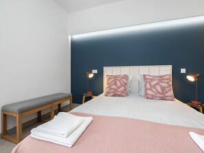 Ein ordentlich eingerichtetes Schlafzimmer mit einem Bett, zwei Nachttischen, einer Bank und einer Nachttischlampe.