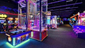 Een helder verlichte speelhal met diverse spelautomaten, waaronder grijpmachines en racegames.
