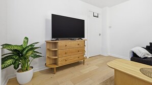 Un salon moderne avec un meuble TV en bois, un grand téléviseur à écran plat, une plante en pot et un canapé.