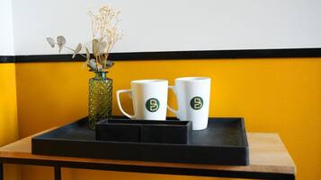 Een tafel met twee witte mokken met een logo, een glazen vaas met gedroogde bloemen, en een zwart dienblad.