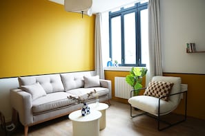 Un salón con sofá, sillón y mesa de centro, una ventana con cortinas y un radiador.