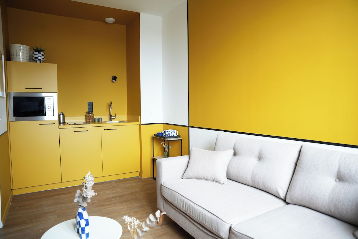 A modern kitchen with yellow cabinets, a white sofa, and a small side table with a blue and white mug.