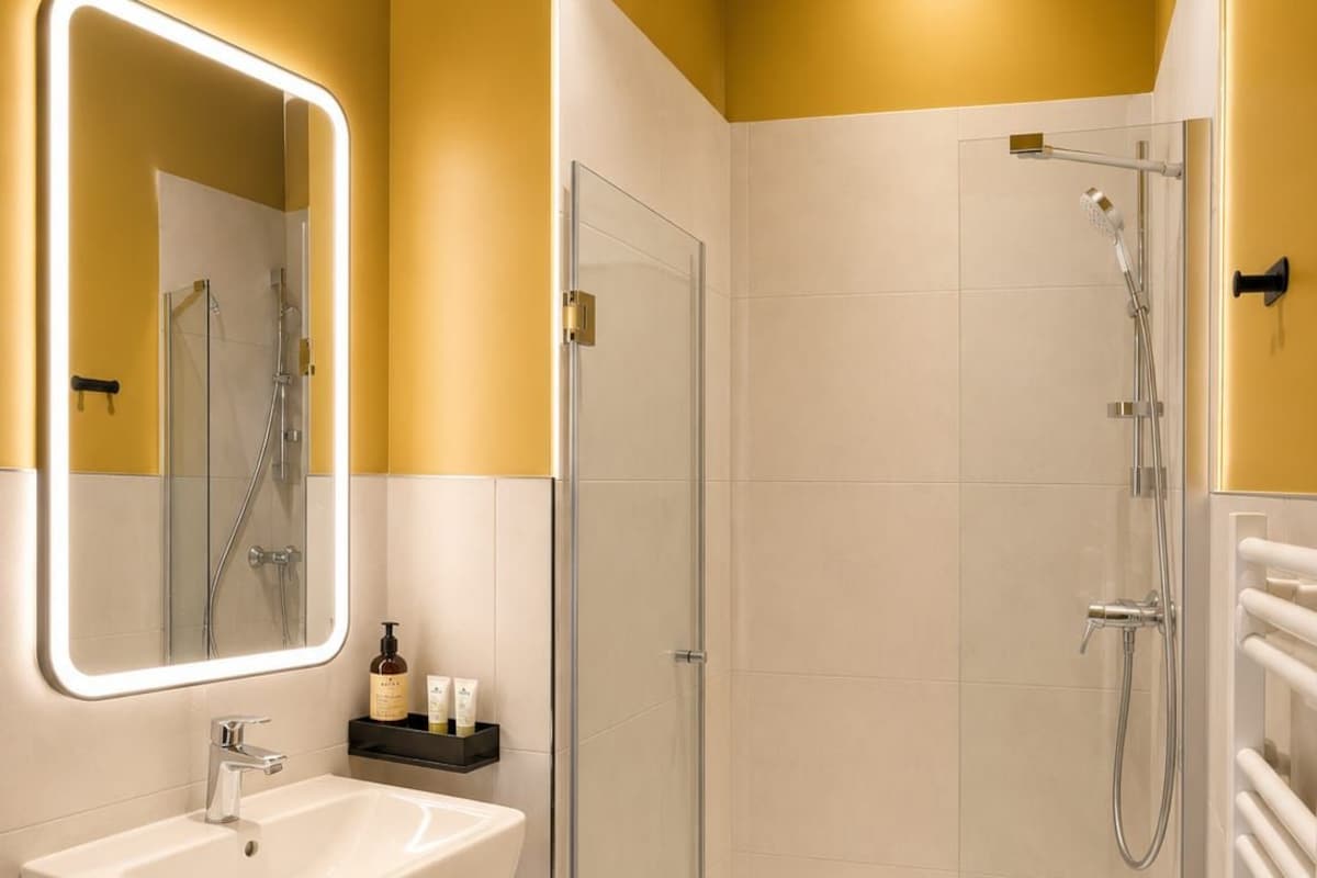 A modern bathroom with a glass-enclosed shower, a white sink with a mirror, and a shelf with toiletries.