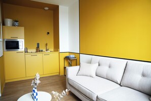 A modern kitchen with yellow cabinets, a white sofa, and a small side table with a blue and white mug. - ARBELLIA (Châlons-en-Champagne)