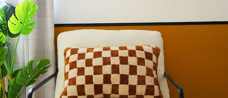 Una silla con un cojín a cuadros, un estante de madera con libros y un florero, y una planta en maceta.