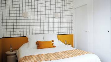 Una cama bien tendida con una manta a cuadros, una mesita de noche con una botella y una pared con un diseño de cuadrícula.