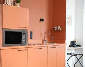 Una cocina con microondas integrado, un lavamanos y un pequeño estante con tazas.