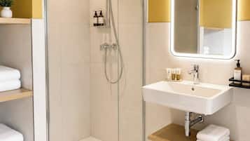 Un baño moderno con ducha de vidrio, un lavabo blanco con espejo y estantes con toallas.