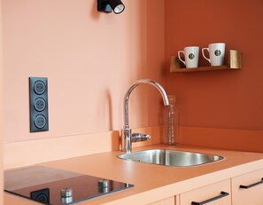 Cocina moderna con pileta de acero inoxidable, estufa integrada y lámpara de pared.