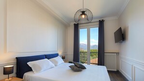 A hotel room with a large bed, a TV mounted on the wall, and a view of the outdoors through a window.