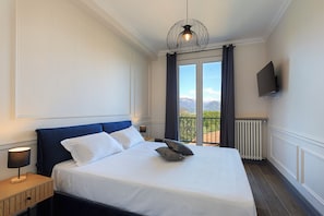 A hotel room with a large bed, a TV mounted on the wall, and a view of the outdoors through a window. - Black Pepper Stresa (Stresa)
