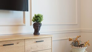 A wooden cabinet with drawers, a television mounted above it, and a vase with dried flowers on the floor.