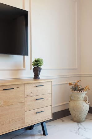 A wooden cabinet with drawers, a television mounted above it, and a vase with dried flowers on the floor. - Black Pepper Stresa (Stresa)