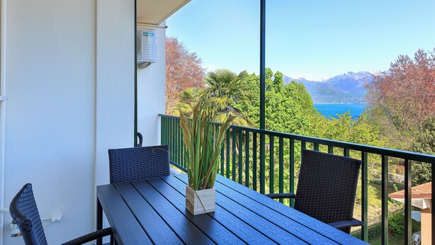 A balcony with a table and chairs, overlooking a scenic view of mountains and a body of water.