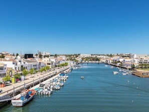 Uma marina com barcos atracados ao longo da orla, uma ponte ao longe e edifícios à beira-mar.