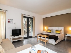 A hotel room with a bed, bedside tables, a TV, a sofa, a small table with a glass, and a view of the outside through a glass door. - Olea White Studio 6, Tavira, Algarve (Querença)