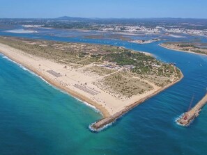 An aerial view of a coastal area with a beach, a small island with buildings, and a pier extending into the water. - Olea White Studio 6, Tavira, Algarve (Querença)