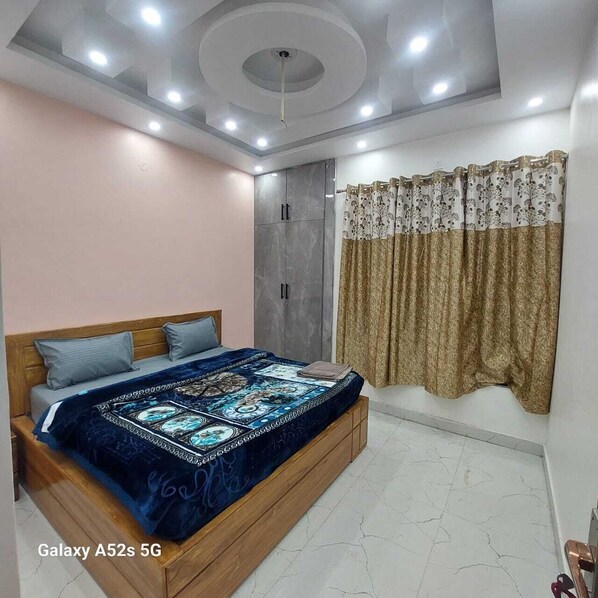 A bedroom with a bed, a wardrobe, a ceiling with recessed lighting, and a window with curtains.