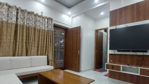 A modern living room with a white sofa, wooden coffee table, and a TV mounted on a wooden panel. - Himalayan View stay Shehar wala ghar (Dehradun)