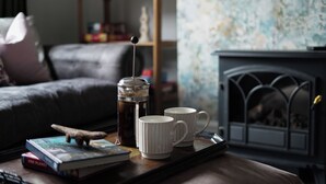 Een gezellige woonkamer met een bijzettafeltje waarop een koffiepot, twee mokken, een boek en een decoratief object staan.